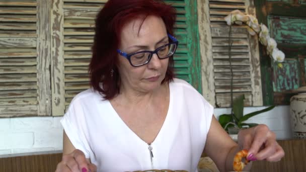 Een vrouw is het eten van garnalen in haar hand bij een restaurant — Stockvideo