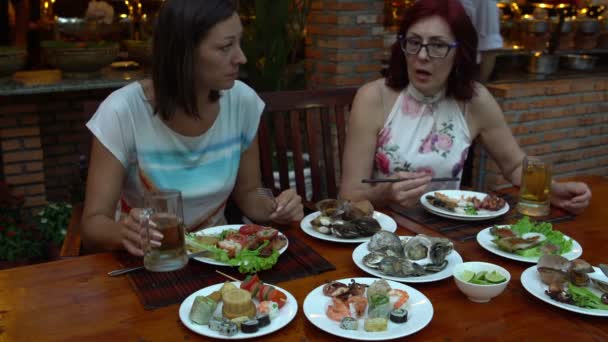 Женщины за столом в ресторане едят морепродукты говорят и пьют пиво — стоковое видео