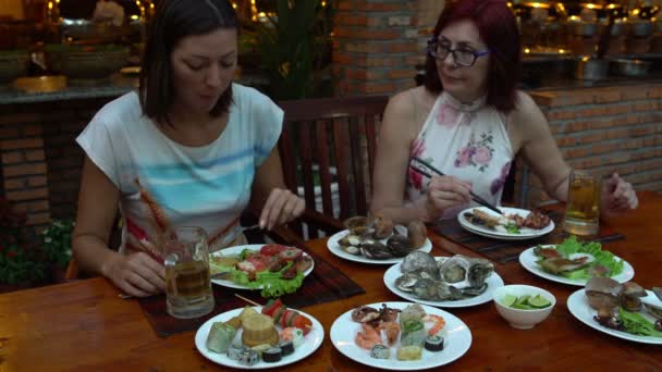 Amigos en una mesa en el restaurante comiendo mariscos hablan tazas de cerveza y bebida — Vídeo de stock