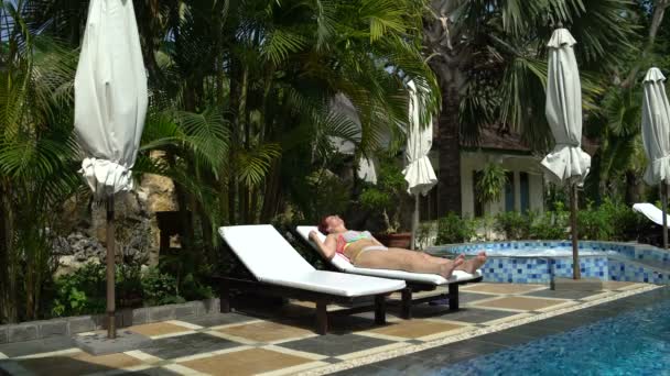 泳池穿泳衣的女人躺在阳光下躺椅和晒黑 — 图库视频影像