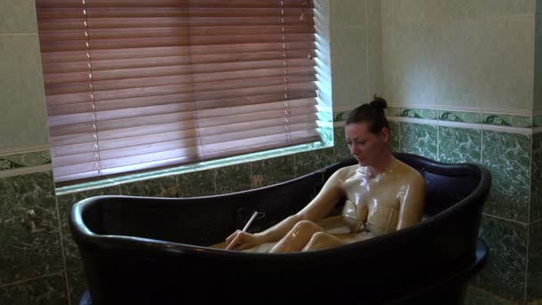 一个女孩坐在泥泞的浴缸里, 给自己倒了一壶泥巴。 — 图库视频影像