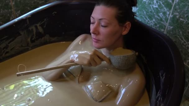 Девушка лежит в грязевой ванне и наливает себе кувшин грязи — стоковое видео
