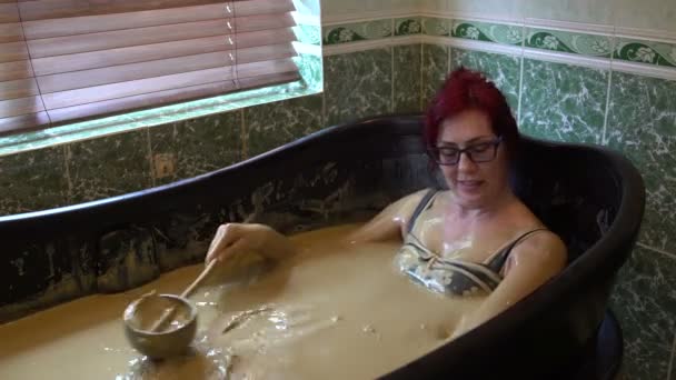 泥風呂で横になっていると、自分に泥の水差しを注ぐ女性 — ストック動画