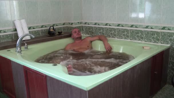 男人躺在按摩浴缸里, 里面有矿泉水和草药。 — 图库视频影像