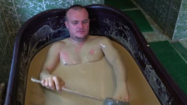 Adam çamur şifa ile bir banyo yer almaktadır ve kendisi kova dışarı dökülen