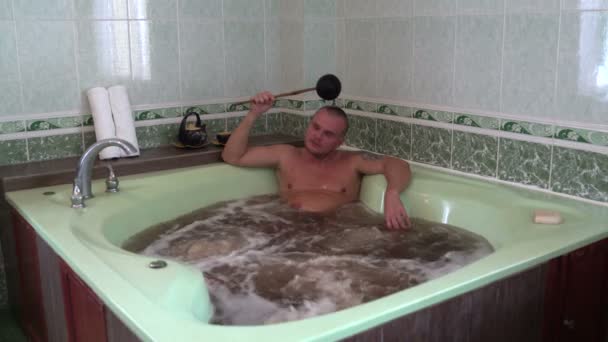 Un homme assis dans un jacuzzi avec des herbes et de l'eau minérale et débordant de la louche — Video