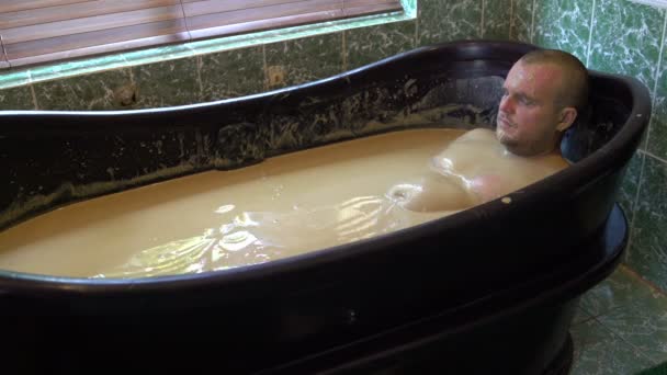 L'homme repose dans un bain de boue thérapeutique et verse de la saleté sur sa tête — Video