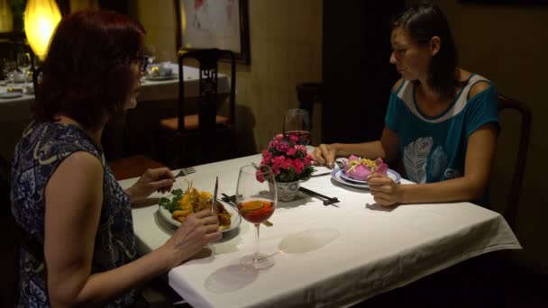 Kvinnor som sitter vid ett bord i restaurangen prata, äta, toast glasögon och dricka rödvin — Stockvideo