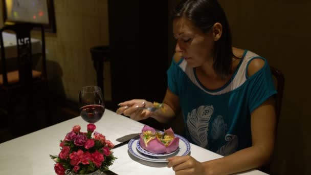 Девушка сидит за столом и ест блюдо в виде цветка лотоса и пьет красное вино — стоковое видео
