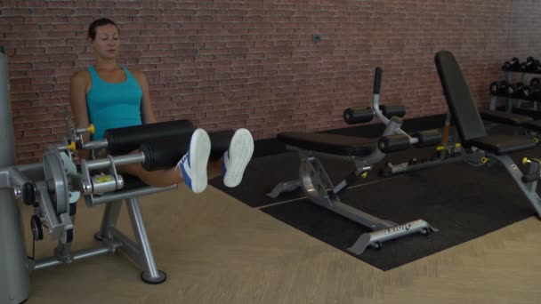 En kvinna på gymmet har en simulator för sittande bensträck — Stockvideo