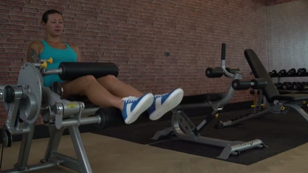 Une femme est au gymnase. Effectue une machine d'exercice pour l'extension des jambes — Video