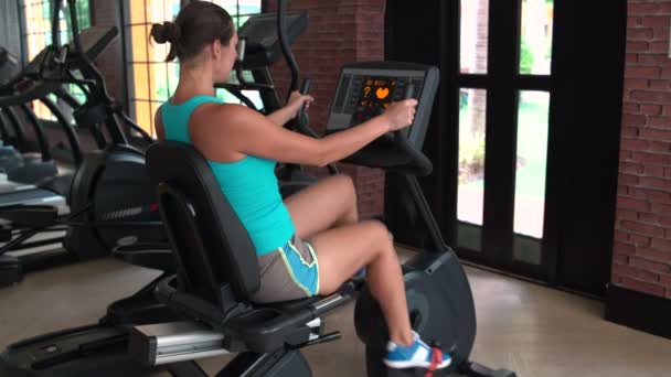 Una mujer tiene en una bicicleta estacionaria — Vídeos de Stock