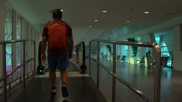 Žena na letišti stojí na elektromotorem. Muž s batohem chodí podél pohyblivých chodníků — Stock video