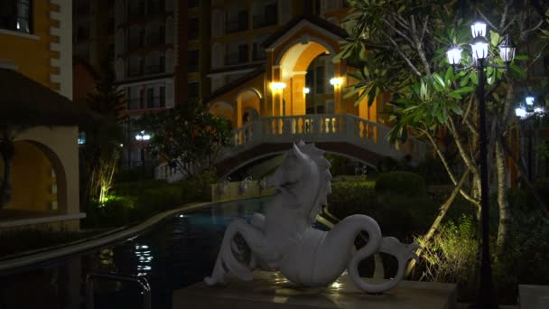 Εξωτερική πισίνα με ένα άγαλμα του Αιγόκερω το βράδυ. Το γεφύρι περνά κορίτσι — Αρχείο Βίντεο