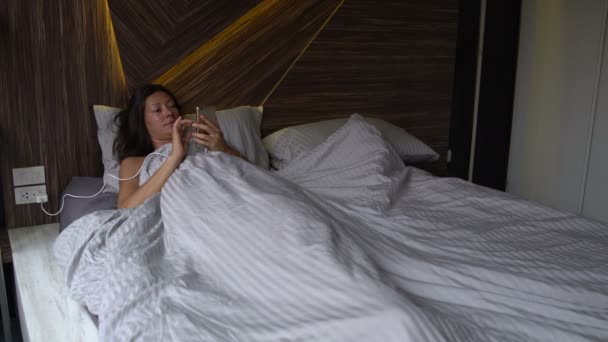 Una mujer se acuesta en la cama y disfruta del Smartphone — Vídeo de stock