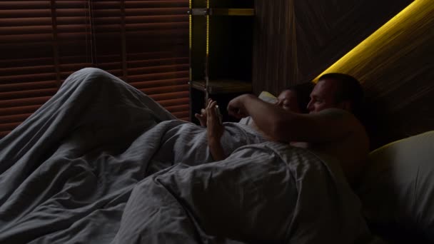 Чоловік і його дружина лежать в ліжку і дивитися смішні відео на вашому телефоні — стокове відео