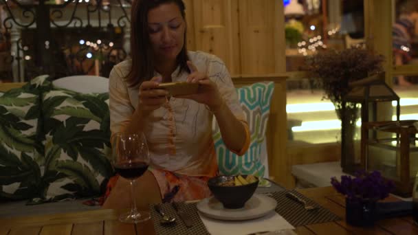 Una mujer en un restaurante hace platos de fotos en el teléfono inteligente — Vídeo de stock