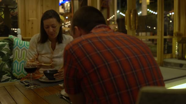 Een man en vrouw zittend in een restaurant, het eten en het drinken van rode wijn — Stockvideo