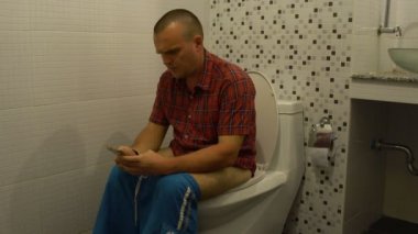 Tuvalet ve kullanan bir akıllı telefon üzerinde oturan bir adam