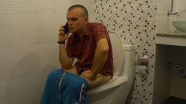 Bir tuvalet ve telefonda konuşurken bir adam oturuyor