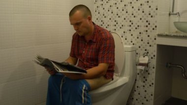Bir adam tuvalette oturmuş ve bir gazete okuyor