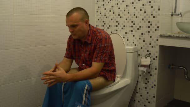 El hombre se sienta en el inodoro, presiona, arranca el papel higiénico y lo usa — Vídeos de Stock