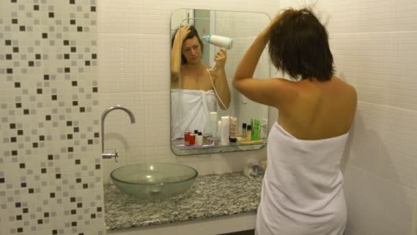 Женщина высушивает волосы перед зеркалом — стоковое видео