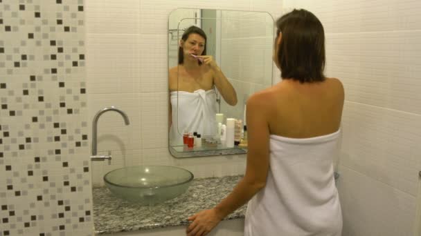 Mujer cepillándose los dientes delante del espejo en el baño — Vídeo de stock