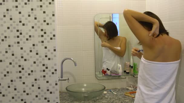 Женщина в полотенце бреет подмышки бритвой перед зеркалом в ванной — стоковое видео