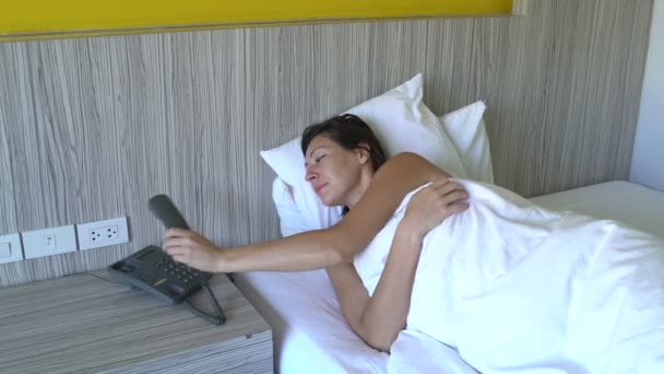 Een vrouw wakker in bed bij de telefoon van het hotel en oproep. — Stockvideo