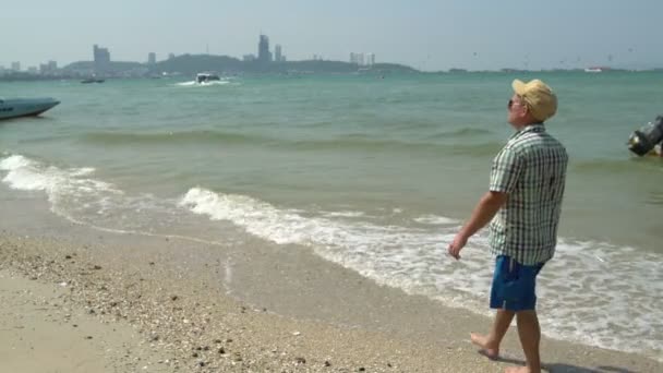一个男人正沿着海边散步 在海浪摇摆小船的海 — 图库视频影像