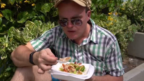 Muž sedí na ulici na parapetu jíst Dušená zelenina z kontejneru