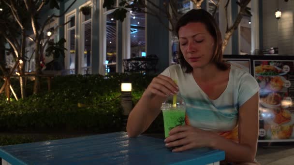 En kvinna dricker bubbla te medan du sitter vid ett bord på ett café på gatan. — Stockvideo