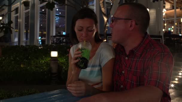 Une femme et un homme boivent du thé moussant assis à une table dans la rue et s'embrassent — Video