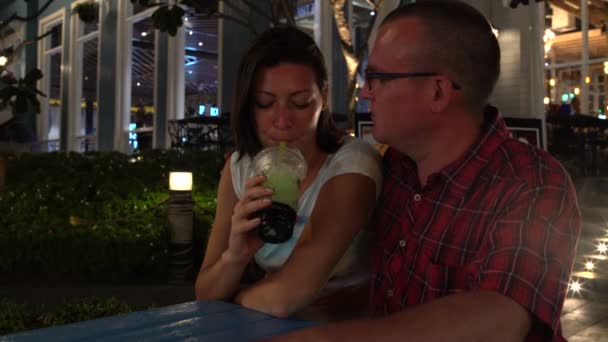Женщина и мужчина сидят за столом на улице, пьют чай с пузырьком и целуются. — стоковое видео