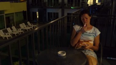 Bir kadın ile bir smartphone bir masada bir otel odası ve sigara balkonda oturuyor