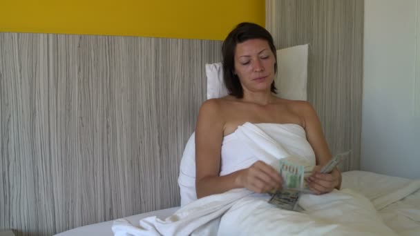 Жінка лежить в ліжку рахує гроші і дає їм — стокове відео