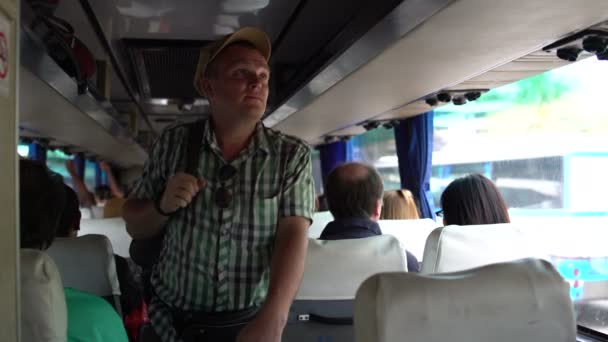 Een man loopt door de cabine van de bus, verwijdert u de tas op de bagagedrager en gaat zitten — Stockvideo