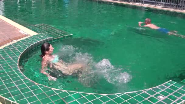 Donna seduta nella vasca idromassaggio. L'uomo nuota in piscina — Video Stock