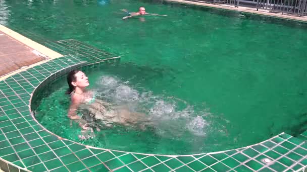 Una mujer está sentada en un jacuzzi. El hombre está nadando en la piscina. — Vídeo de stock