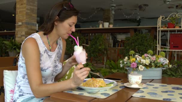 En kvinna sitter vid ett bord i en restaurang äta khao phat och dricka en milkshake — Stockvideo