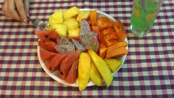 På bordet är en platta av frukt. Kvinnlig hand tar papaya med en gaffel — Stockvideo