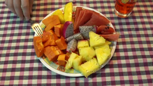 Na mesa está um prato de fruta. Uma mão de homem toma um pityahya com um garfo — Vídeo de Stock