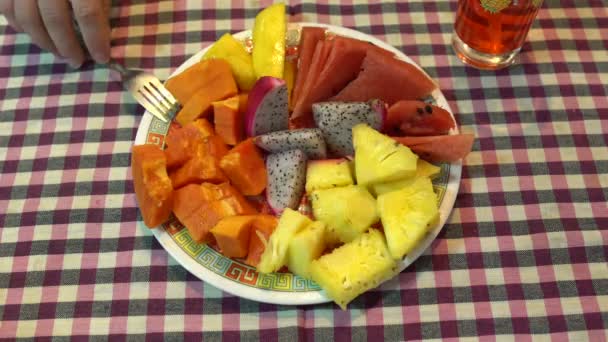 En la mesa hay un plato de fruta. Mano masculina toma papaya con un tenedor — Vídeo de stock