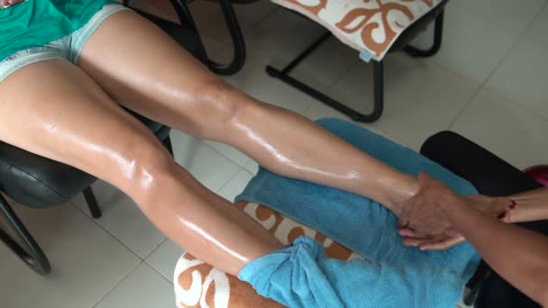 Thai foot massage. The masseuse massages the leg of a woman sitting in a chair. — Stock Video