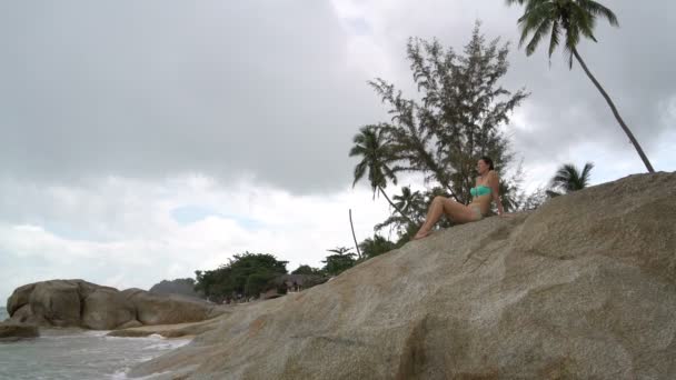 Γυναίκα σε ένα κοστούμι λουσίματος κάθεται σε έναν βράχο δίπλα στη θάλασσα — Αρχείο Βίντεο