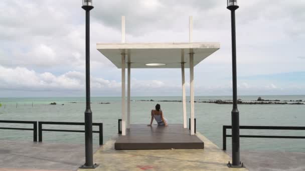 Жінка сидить на пірсі і дивиться на море — стокове відео