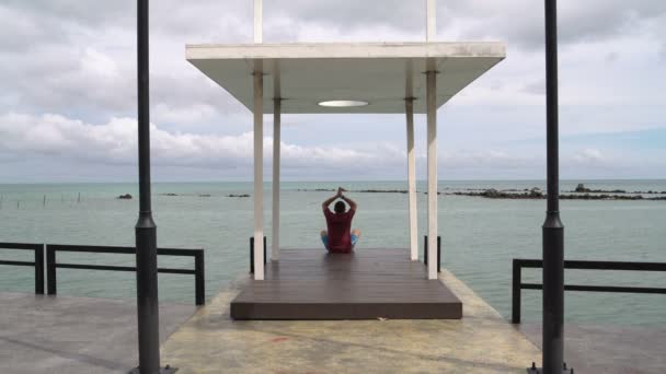 Een man die mediteren zittend op een pier door de zee — Stockvideo