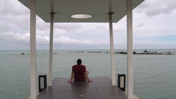 El hombre mira el mar sentado en el muelle — Vídeo de stock
