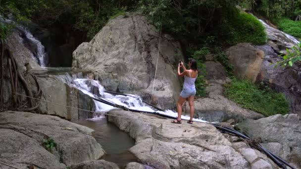 Una mujer fotografiando una cascada — Vídeo de stock